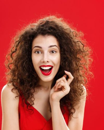 impressed-excited-feminine-adult-woman-with-curly-hair-red-lipstic-elegant-evening-dress